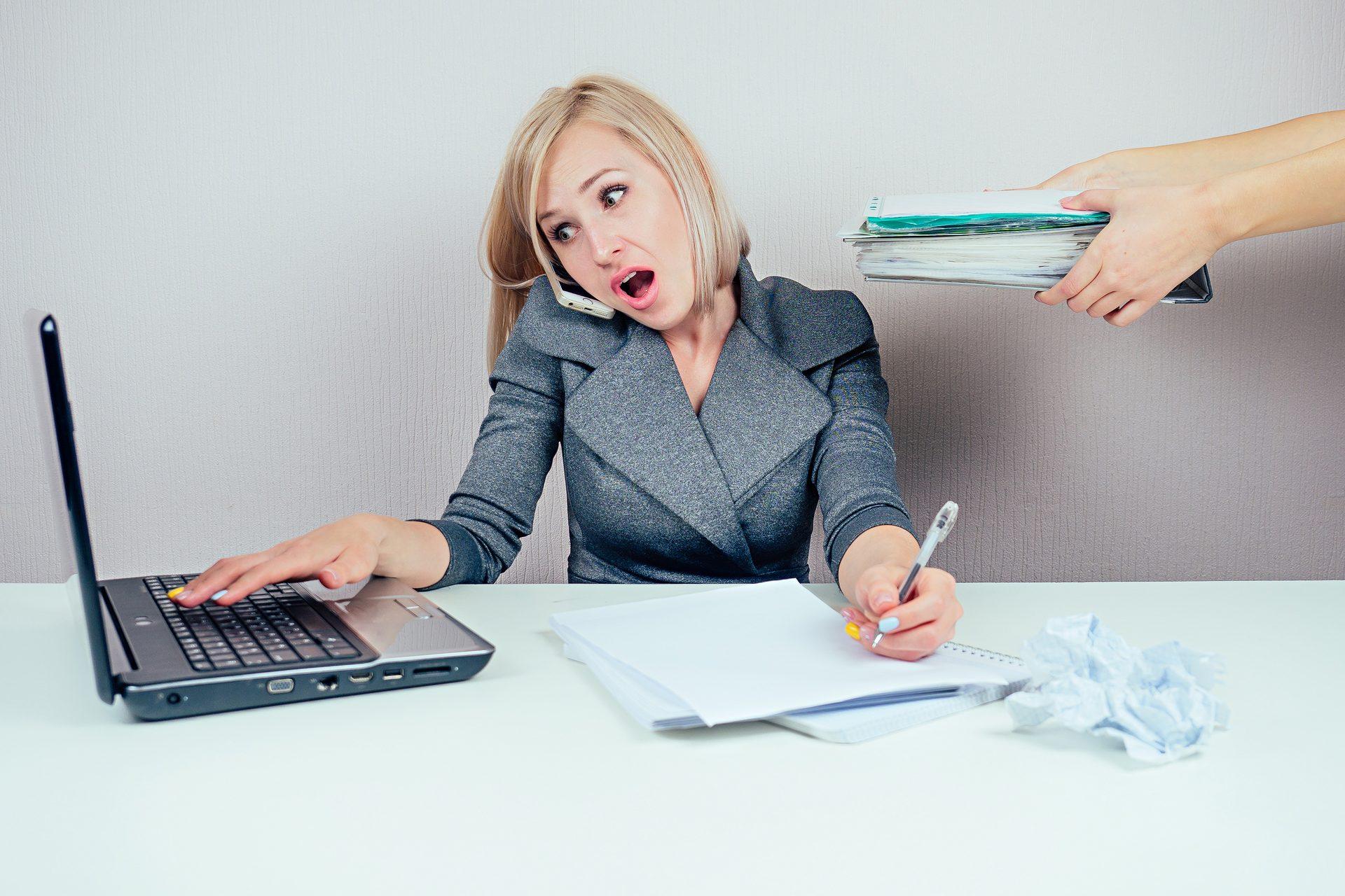 Bizneswoman w garniturze pracuje przy laptopie, trzymając foldery i rozmawiając przez telefon.